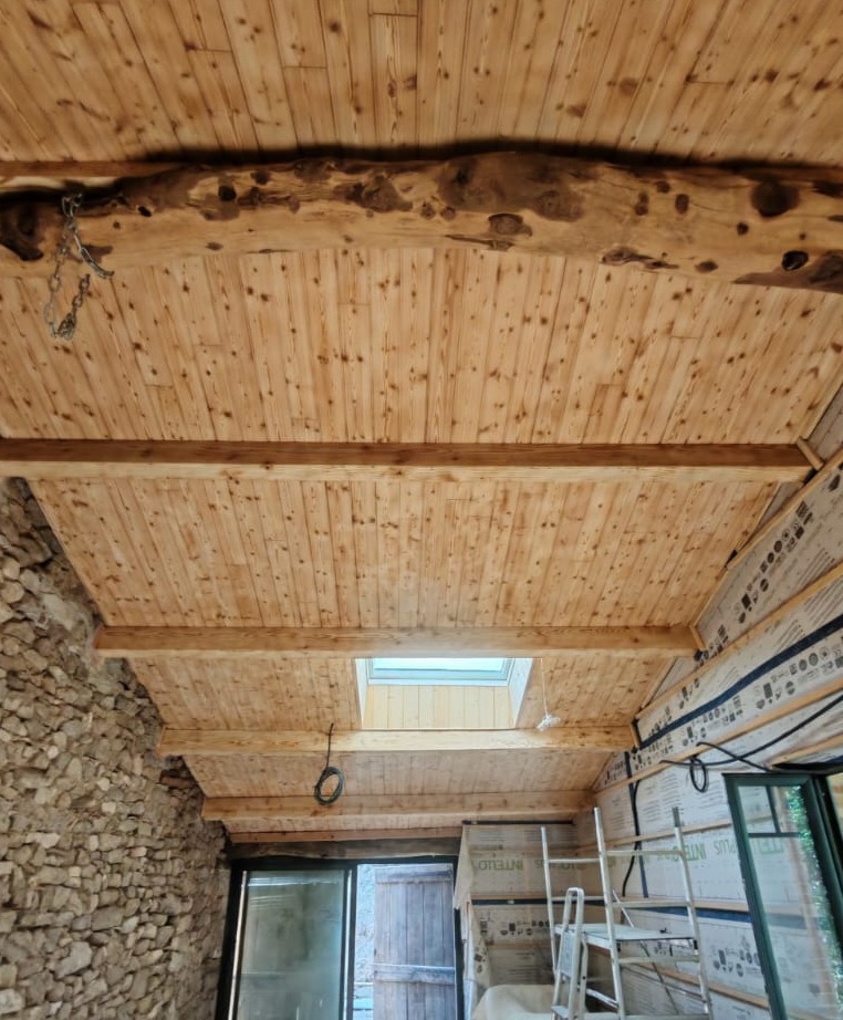 Plafond à poutres éclairci par aérogommage, entre des murs en pierre